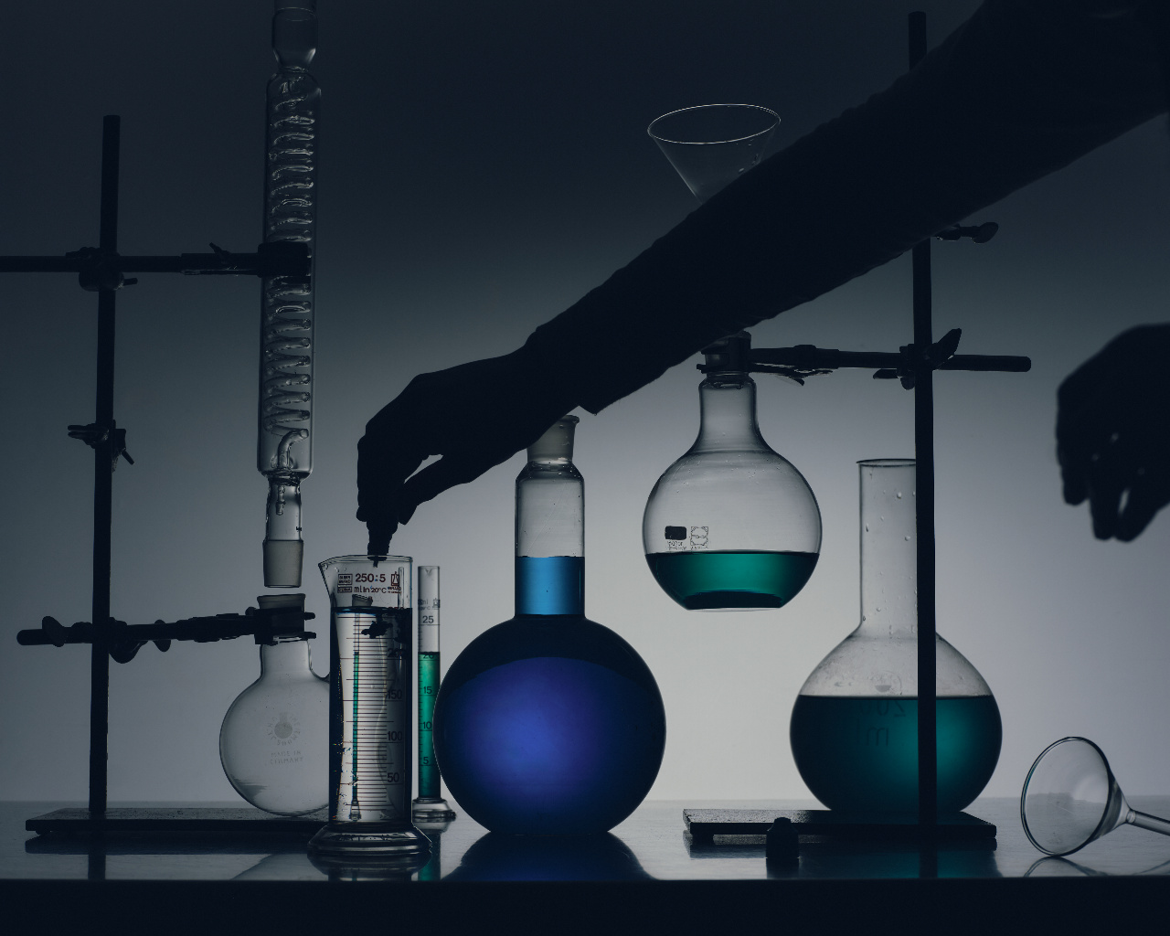 Silhouetted hands working with laboratory flasks filled with blue and green liquids