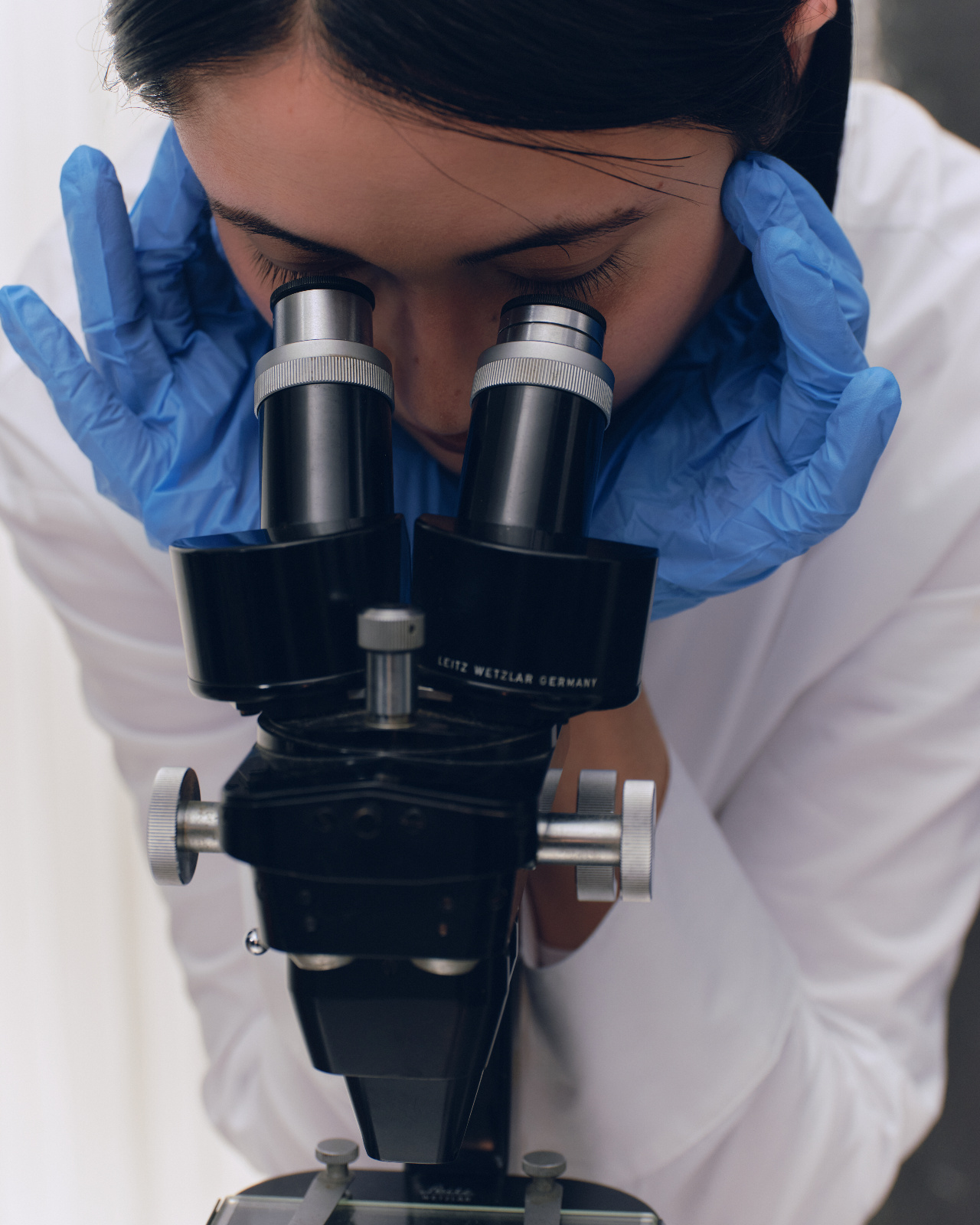 A medical student in a white coat looking into a microscope