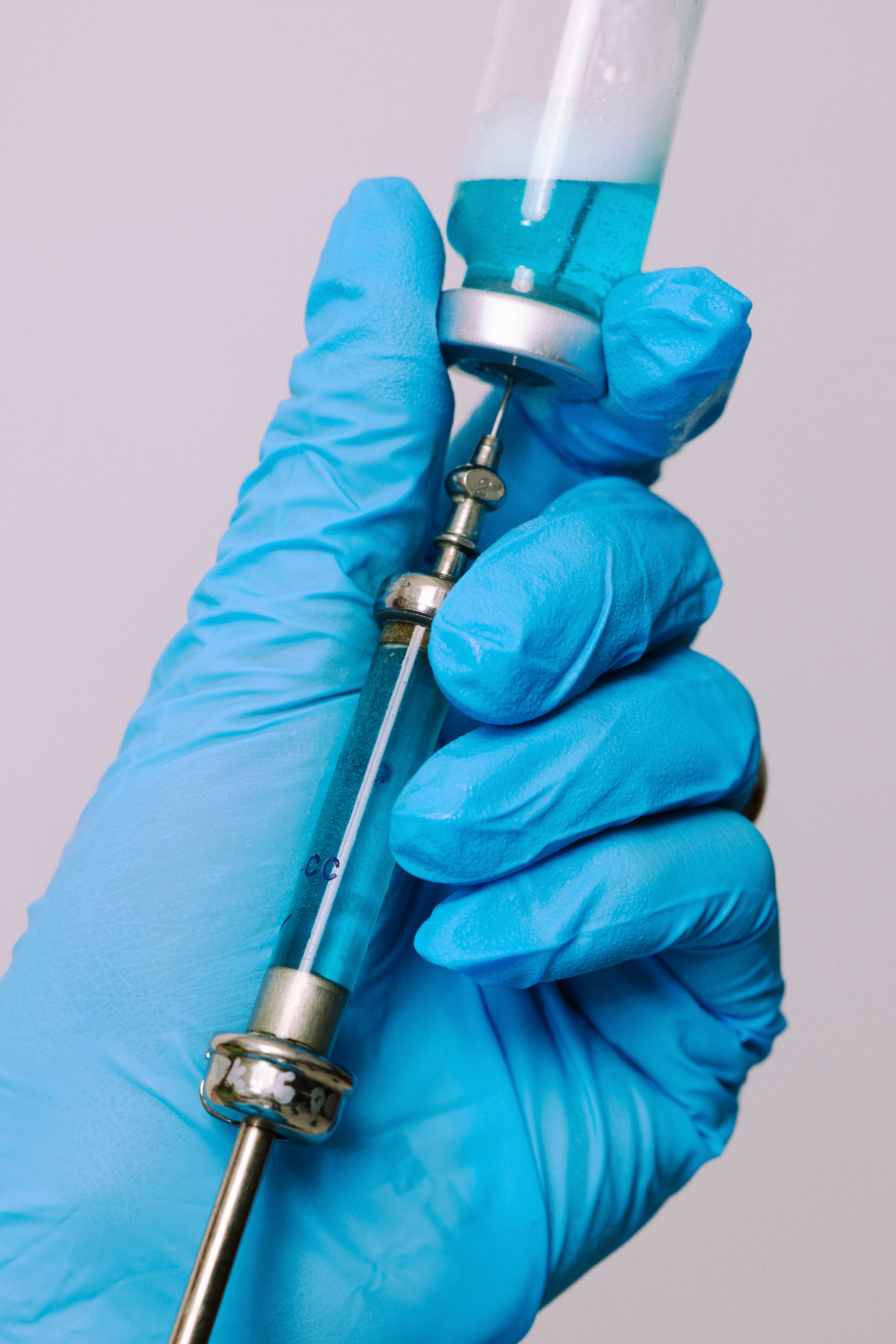 A gloved hand drawing liquid from a vial into a vintage glass syringe